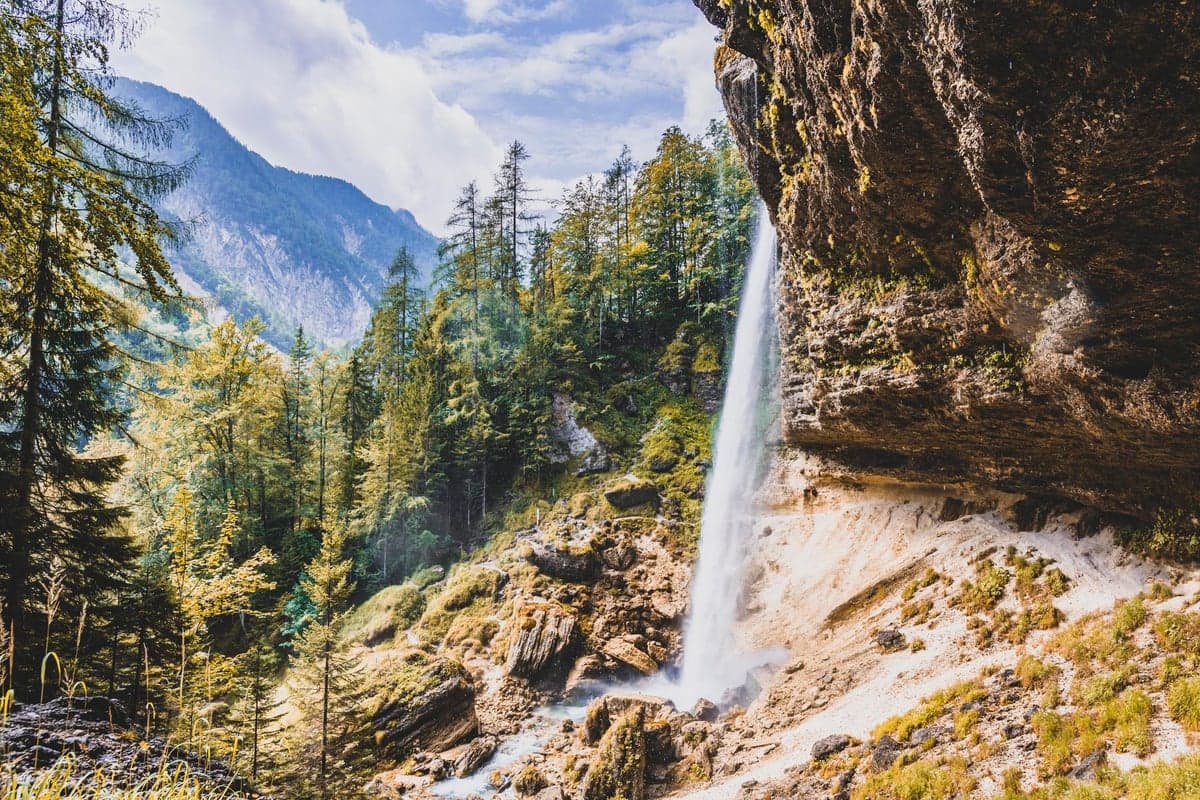 Ein Wasserfall stürzt durch eine bewaldete Alpenschlucht